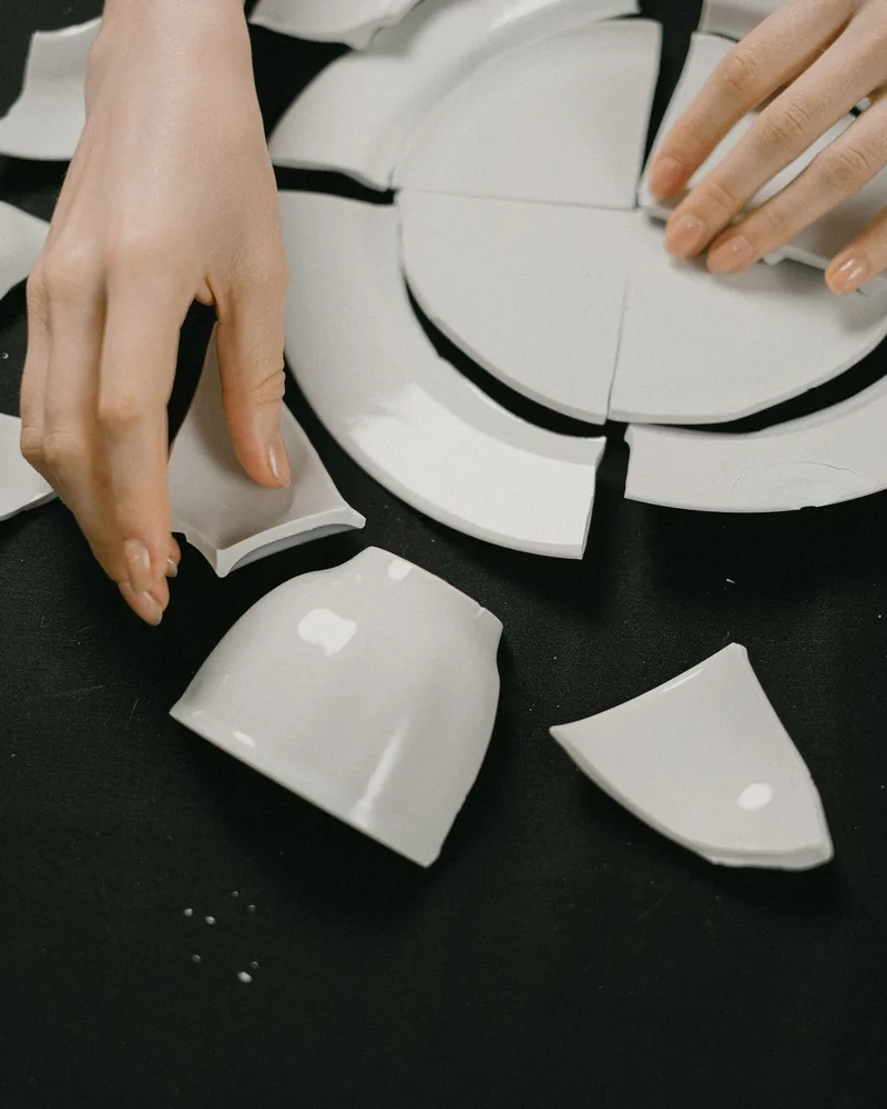 Manos ordenando sobre una superficie oscura los fragmentos de un plato de porcelana roto antes de pegarlo
